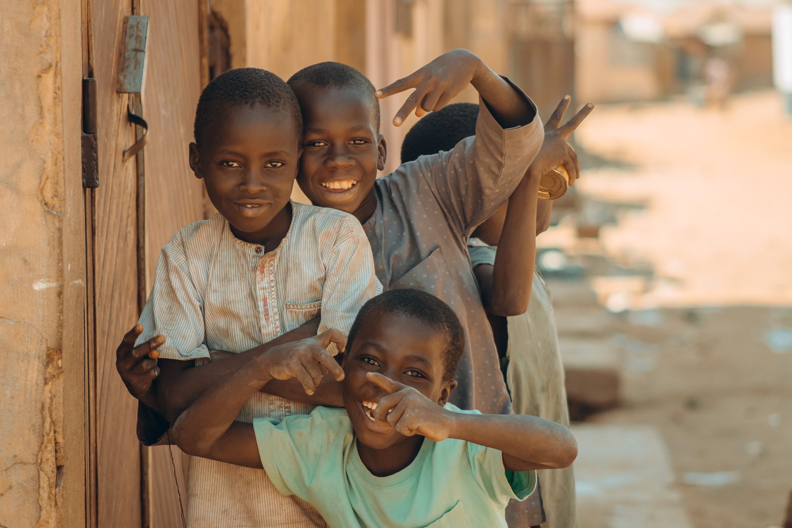 Four boys laughing together in a sunny doorway.