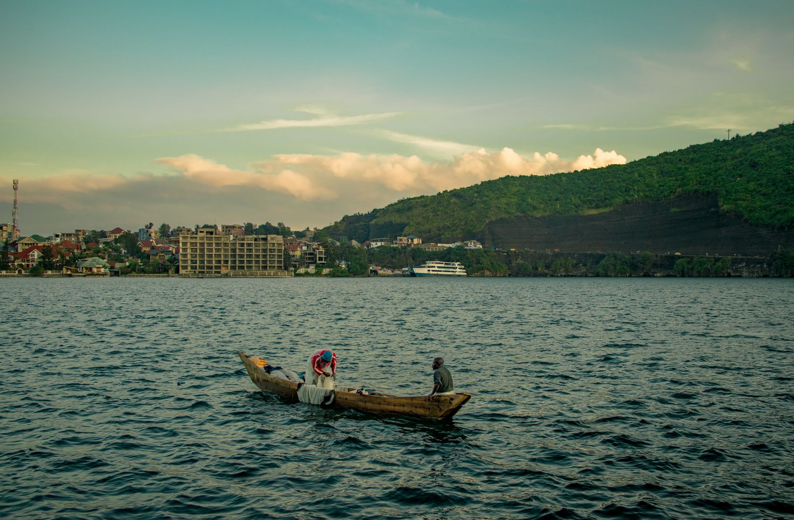 Two fishermen in a wooden canoe on Lake Kivu, the hills of Goma behind them.