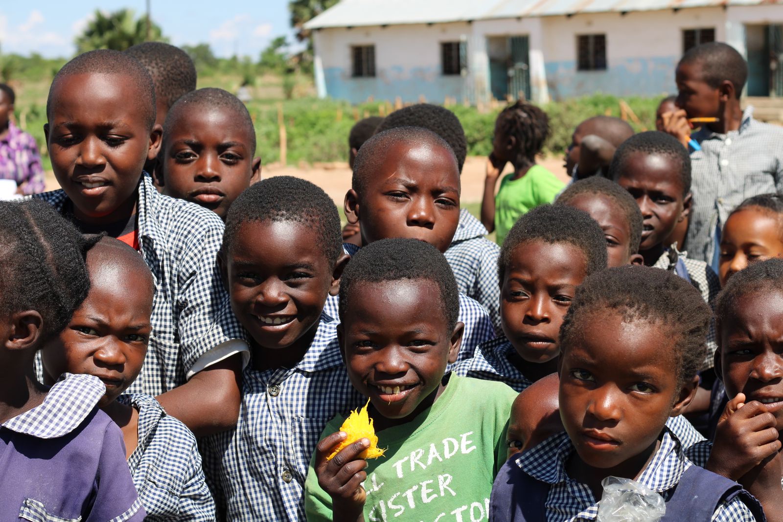 A crowd of smiling schoolchildren in checked uniforms gathers close to the camera.